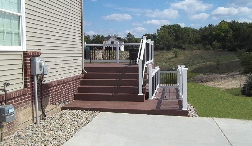 Backyard deck with maroon stairs, white railings, and a concrete patio beside a house