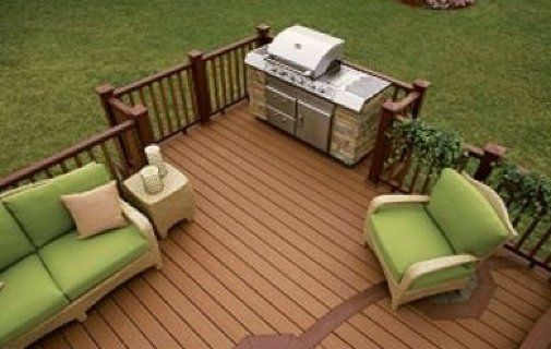 Outdoor deck with green patio sofas, a grill, and wooden railing on a grassy lawn. Outdoor deck with green patio sofas, a grill, and wooden railing on a grassy lawn.