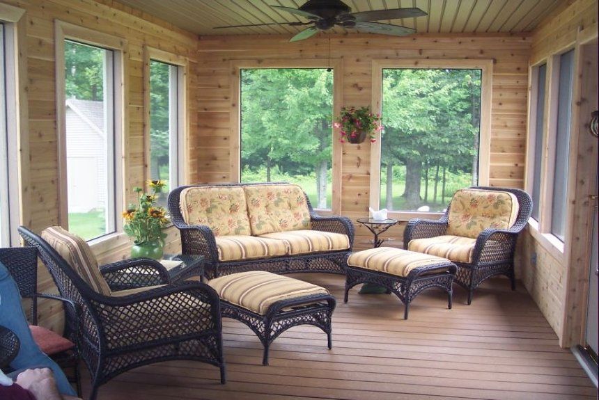 Covered porch seating area with wicker chairs, patterned sofa, and ottoman overlooking a green yard Covered porch seating area with wicker chairs, patterned sofa, and ottoman overlooking a green yard