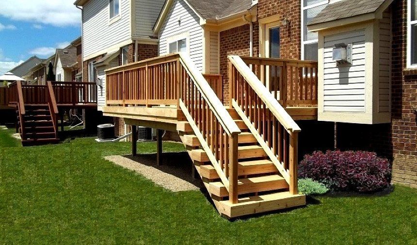Wooden porch stairs and deck on the back of a townhouse, beside a green lawn