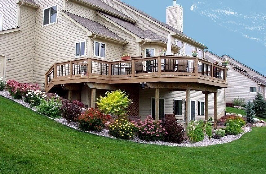 Suburban house with a large wooden deck, landscaped garden, and green sloped lawn