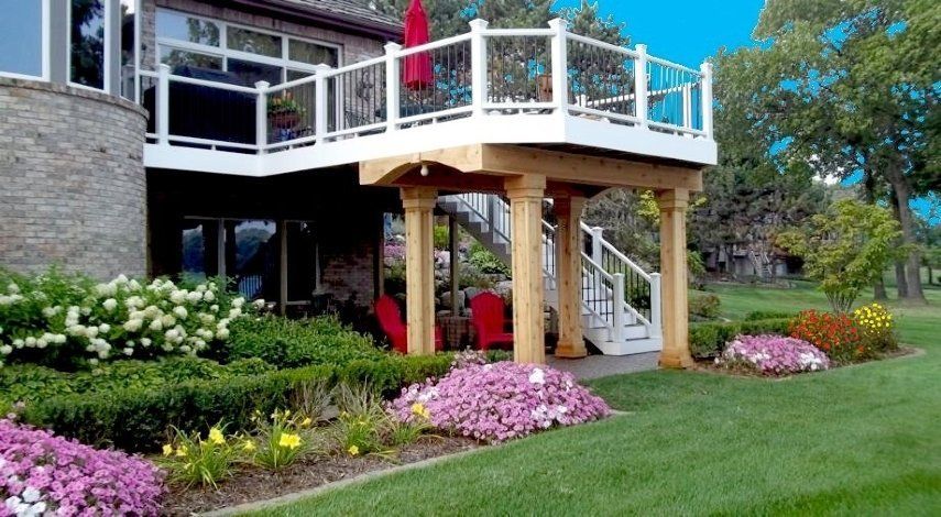 House deck with white railing, red umbrella, flower beds, and a green lawn in a landscaped yard