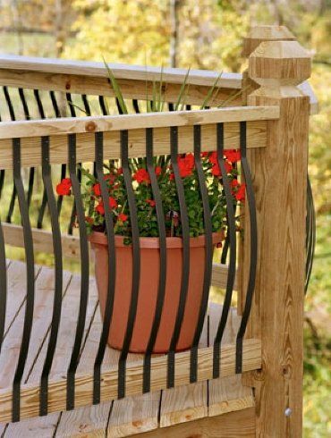Potted red flowers on a wooden deck railing with vertical black balusters