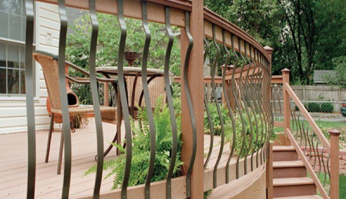 Curved wooden deck with vertical rope railing and stairs, surrounded by green trees and shrubbery.