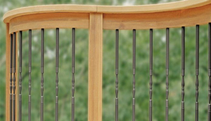 Wooden deck railing with vertical black balusters against a blurred green background