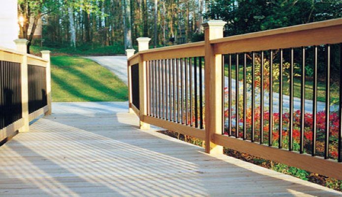 Wooden pedestrian bridge with black railings leading to a landscaped garden path in a wooded park