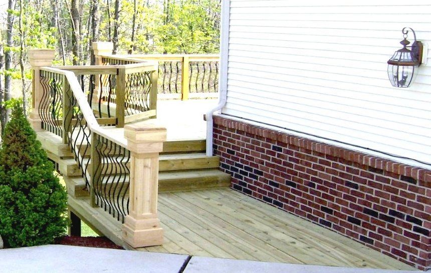 Wooden deck with steps, railing, and red brick foundation beside a white house