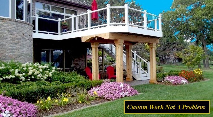 Modern two-story deck with white railings over a garden of pink flowers beside a stone house