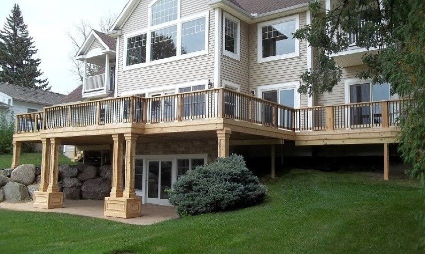 Raised wooden deck attached to a beige house with large windows and a grassy yard