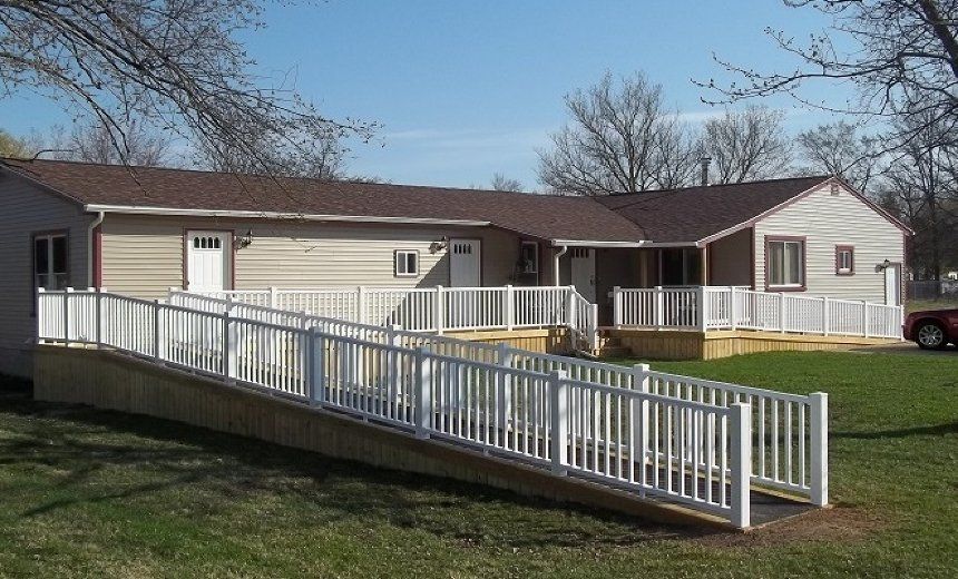 Single-story beige house with white accessibility ramp and railings in a grassy yard.