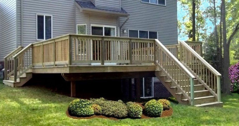 Wooden wraparound deck with stairs on the back of a gray house, above a landscaped yard.
