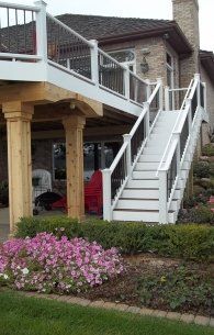 Exterior staircase leading to a second-floor deck on a brick home with pink flowers in front