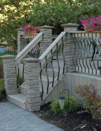 Stone staircase with metal railings leading to a garden patio, with flowers and trees in the background