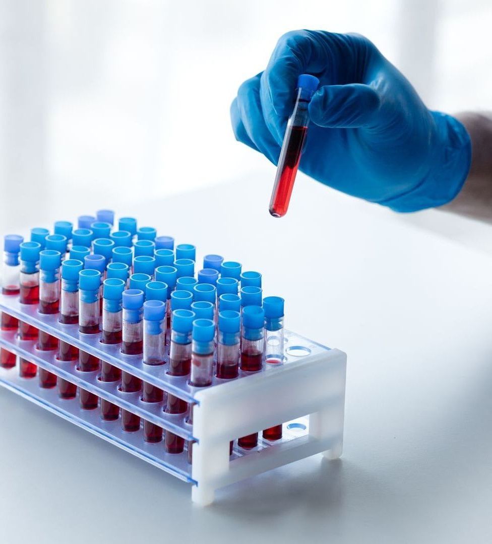 A person in blue gloves is holding a pipette over a rack of test tubes