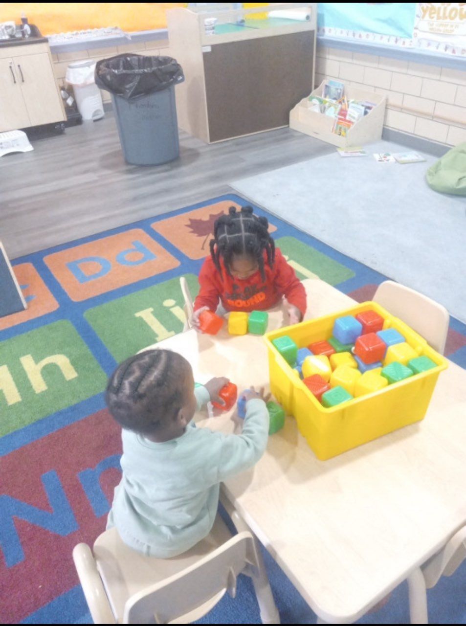 Two children are sitting at a table playing with blocks
