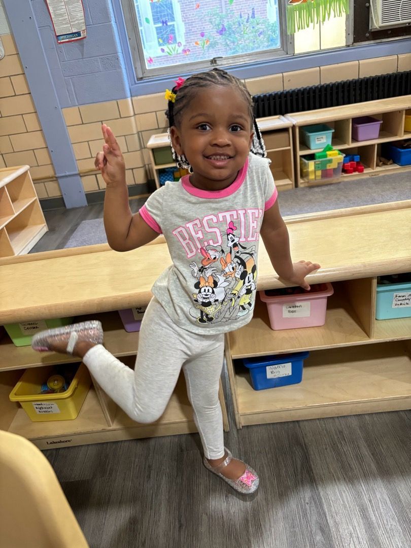 A little girl is standing on one leg in a classroom.