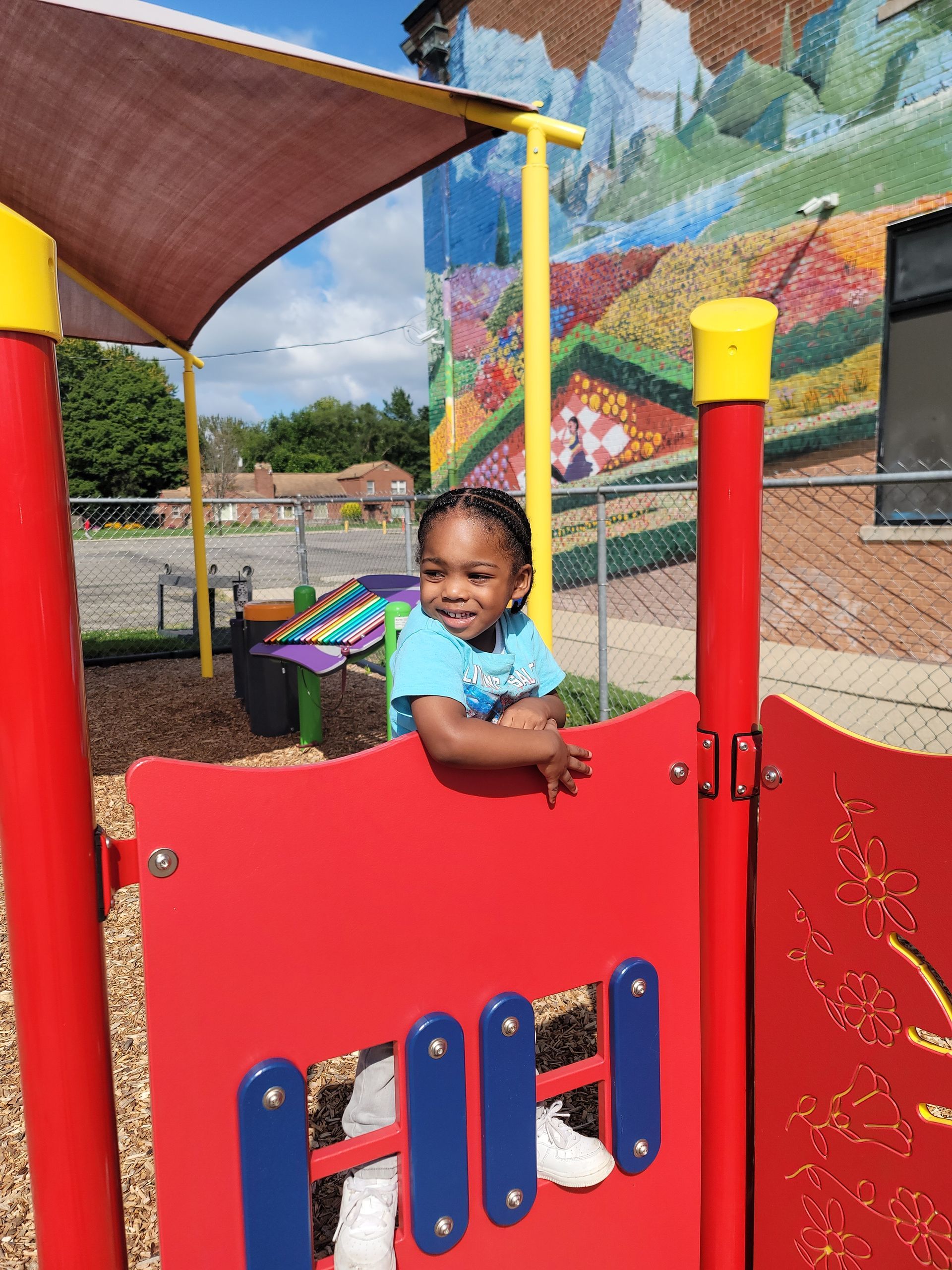 A little girl is playing in a playground with a mural in the background.