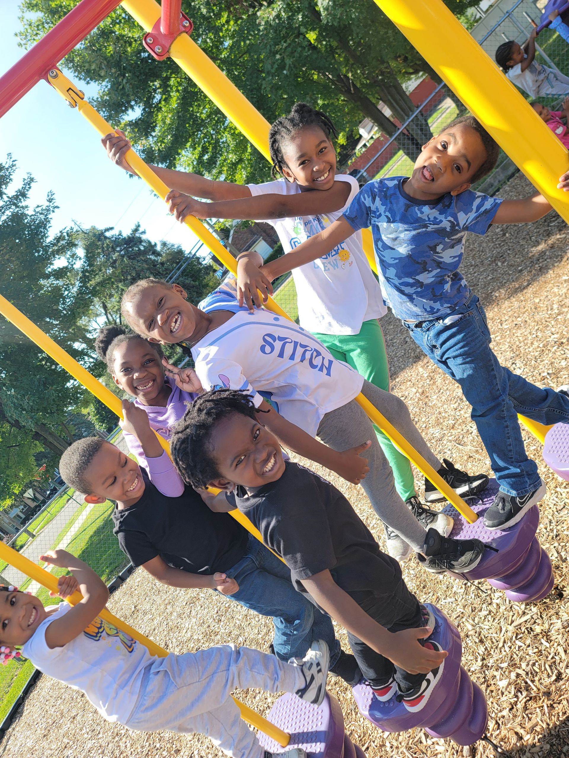 A group of children are playing on a swing set with one wearing a shirt that says stitch