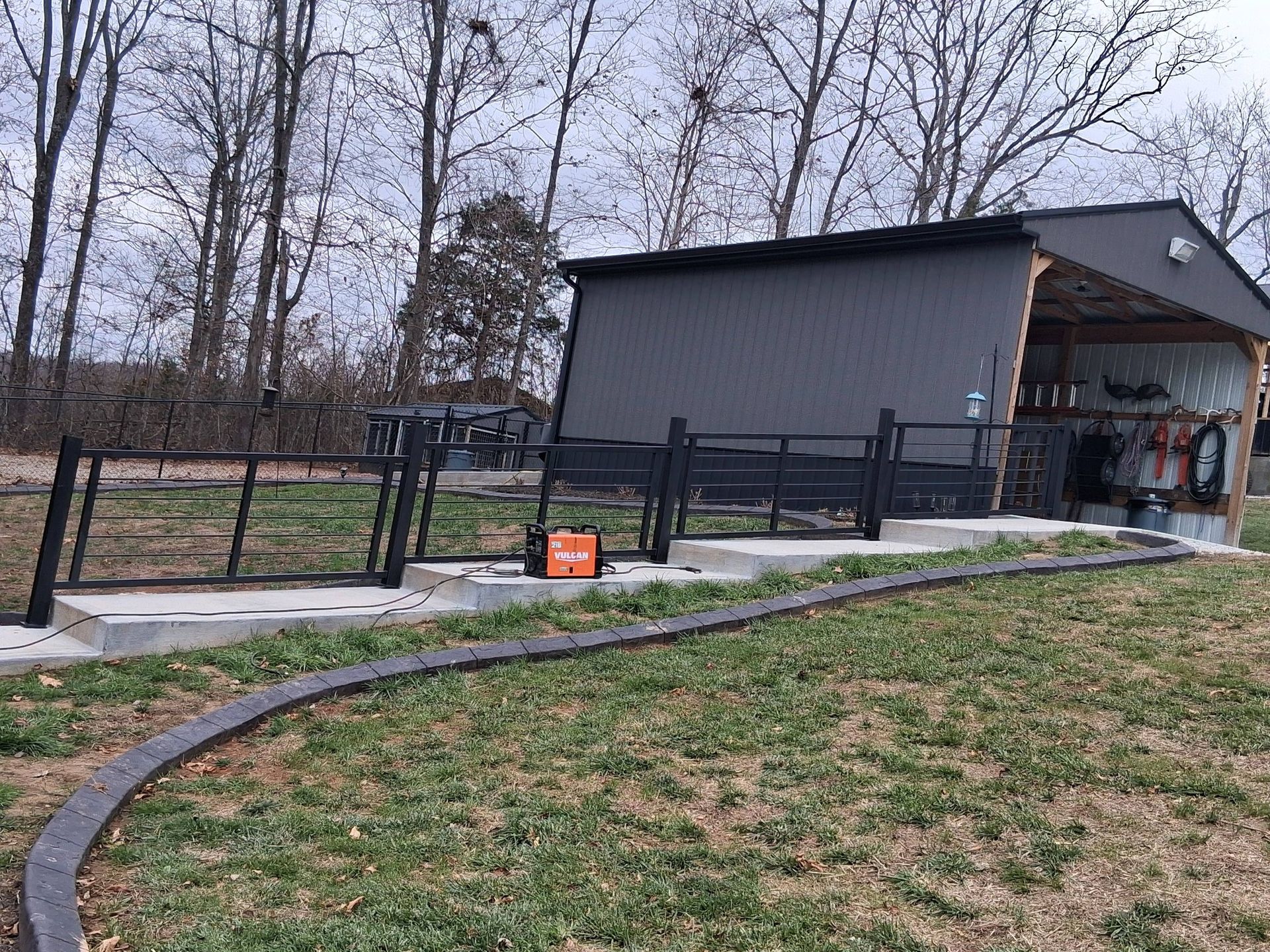 Outdoor pavilion with a curved black track and black fence on a concrete base. An orange object sits on the concrete.