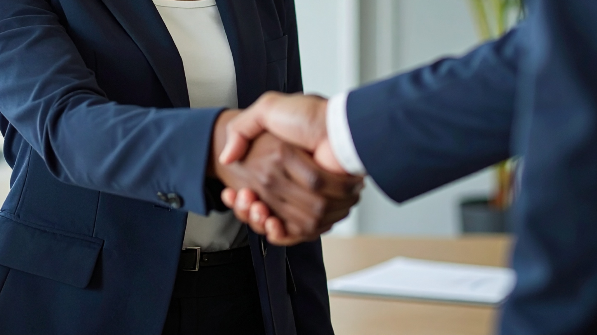 Two business people in suits shaking hands in an office