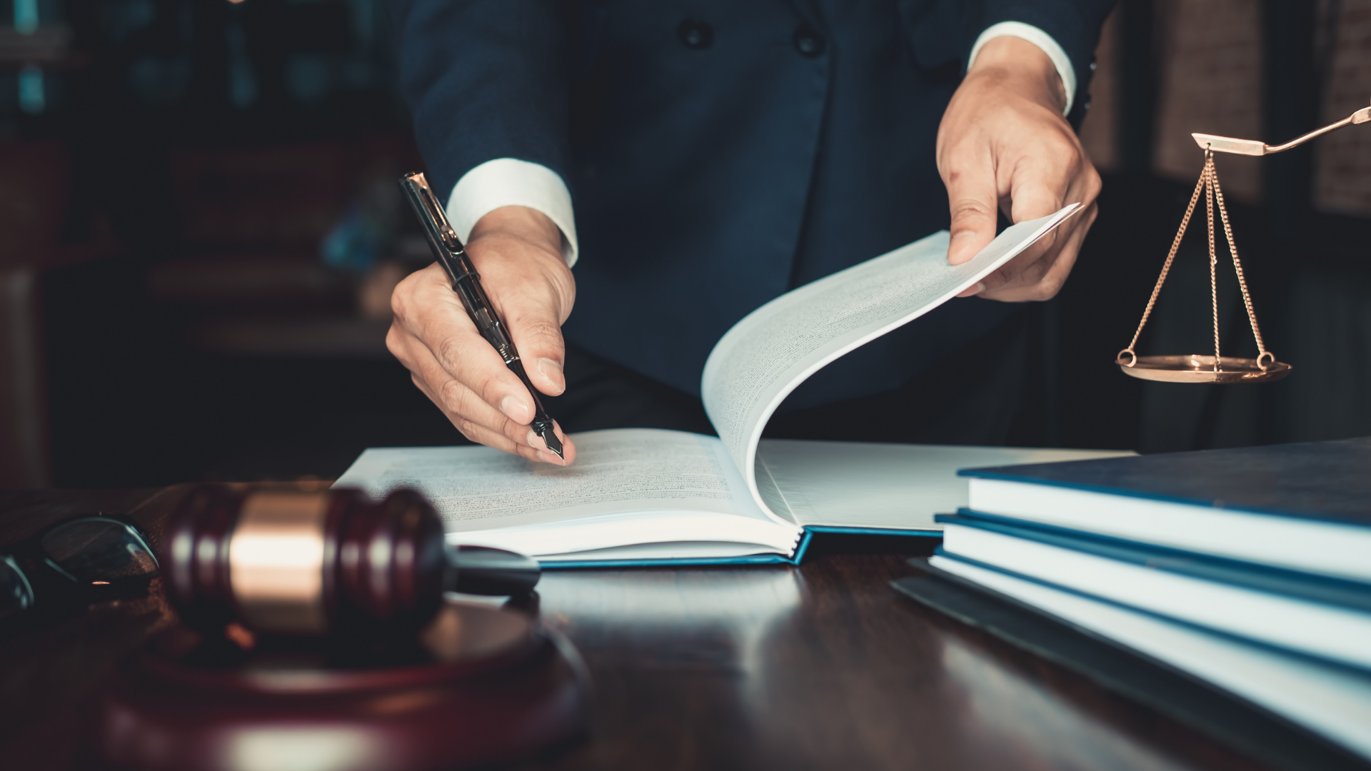 Lawyer hands turn pages in a legal book beside a gavel and scales of justice