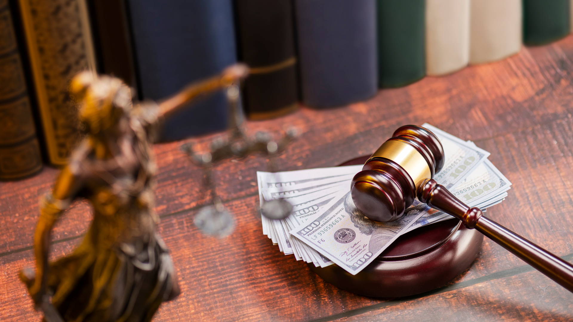 Judge’s gavel on a wooden desk with scattered dollar bills and blurred books in the background