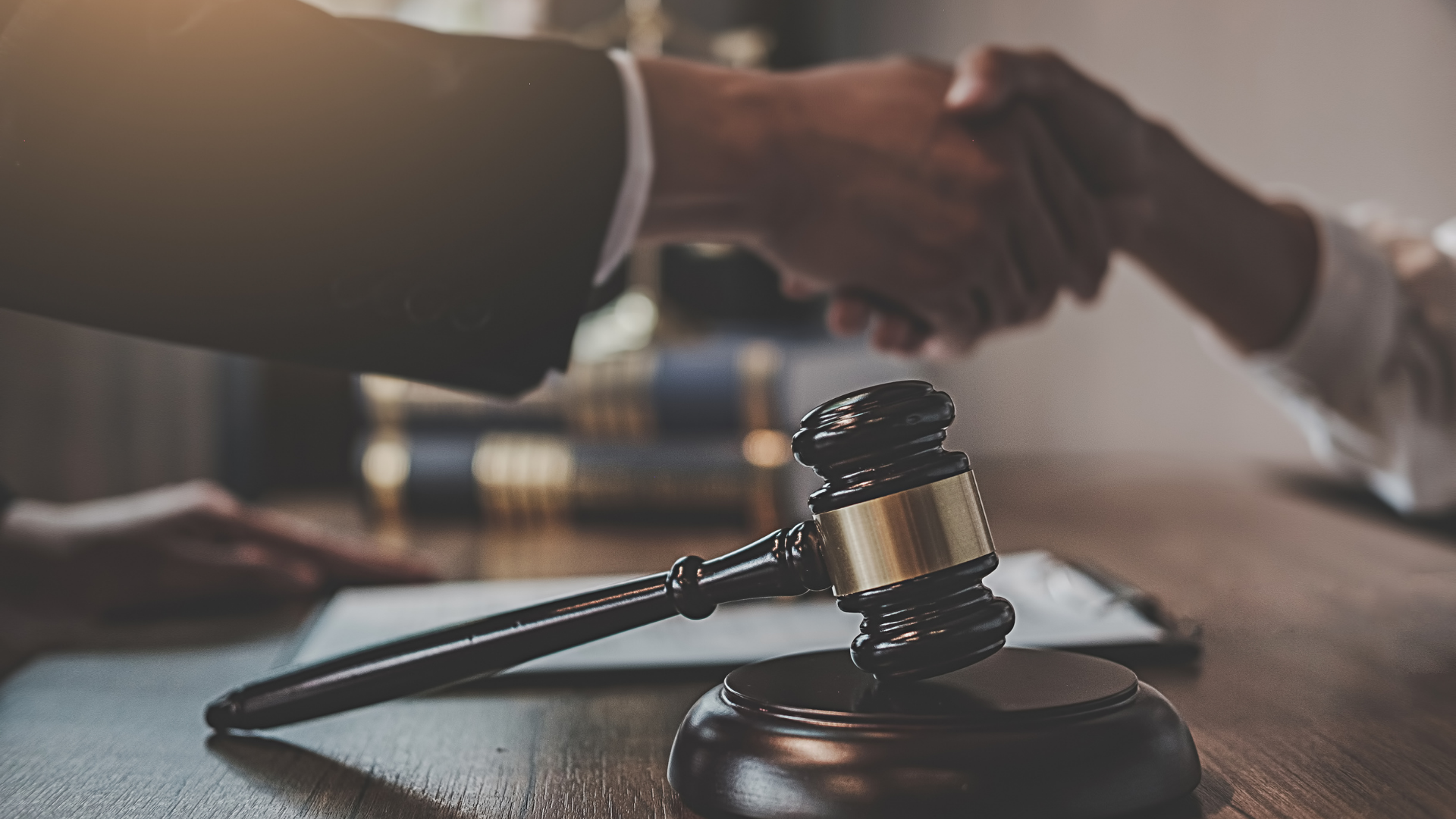Two people shake hands over a desk with a judge’s gavel in the foreground.
