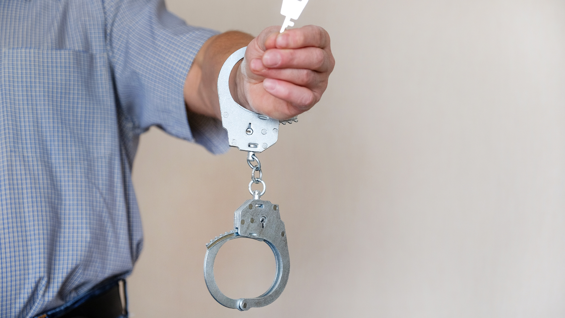 A hand holding a pair of handcuffs against a plain background