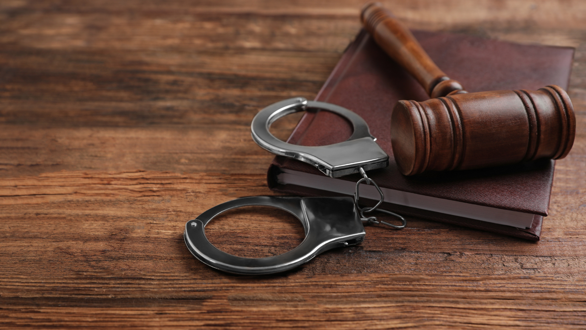 Handcuffs and a judge’s gavel on a brown leather book over a wooden table