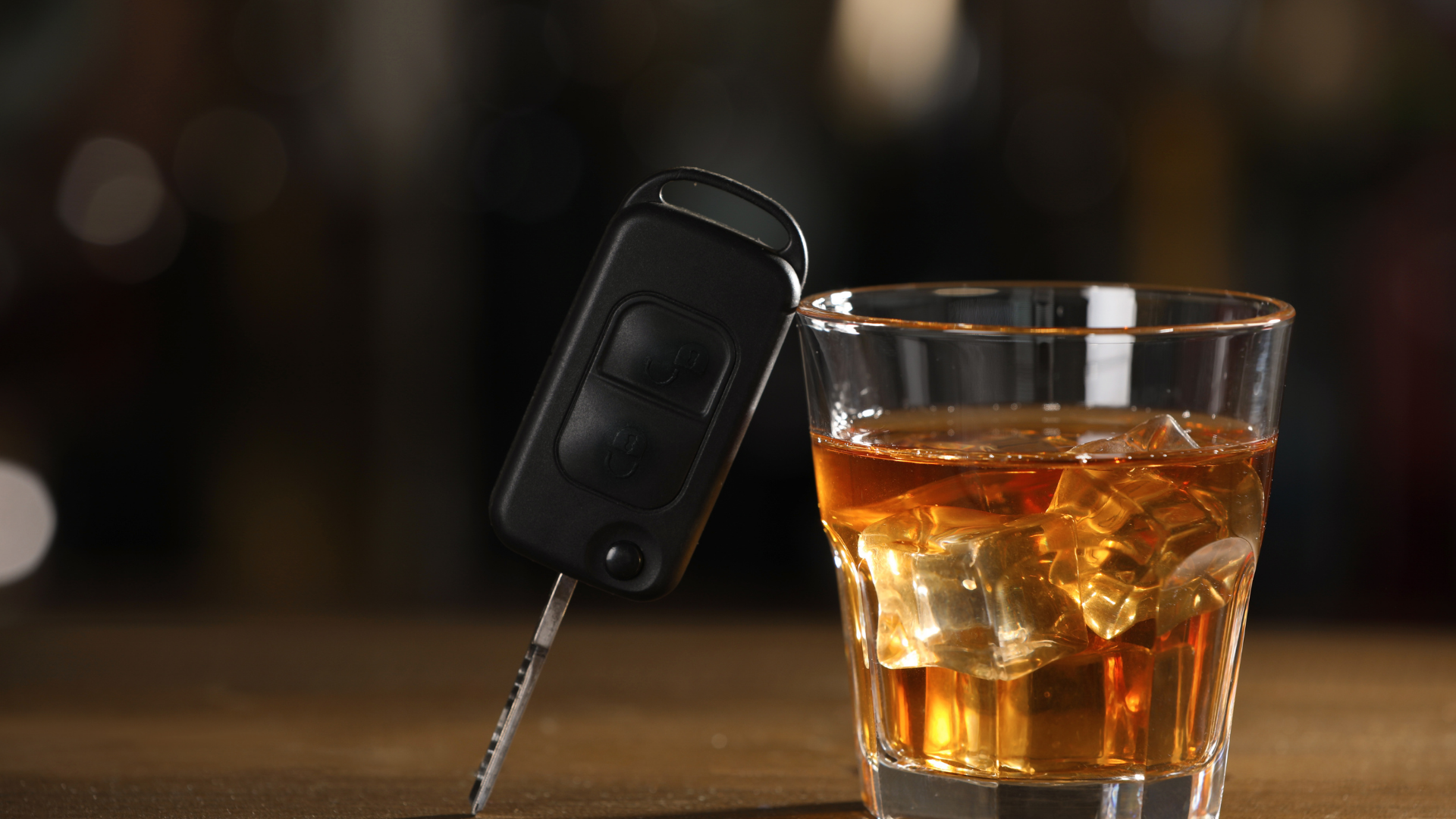A car key fob beside a glass of whiskey on a bar counter