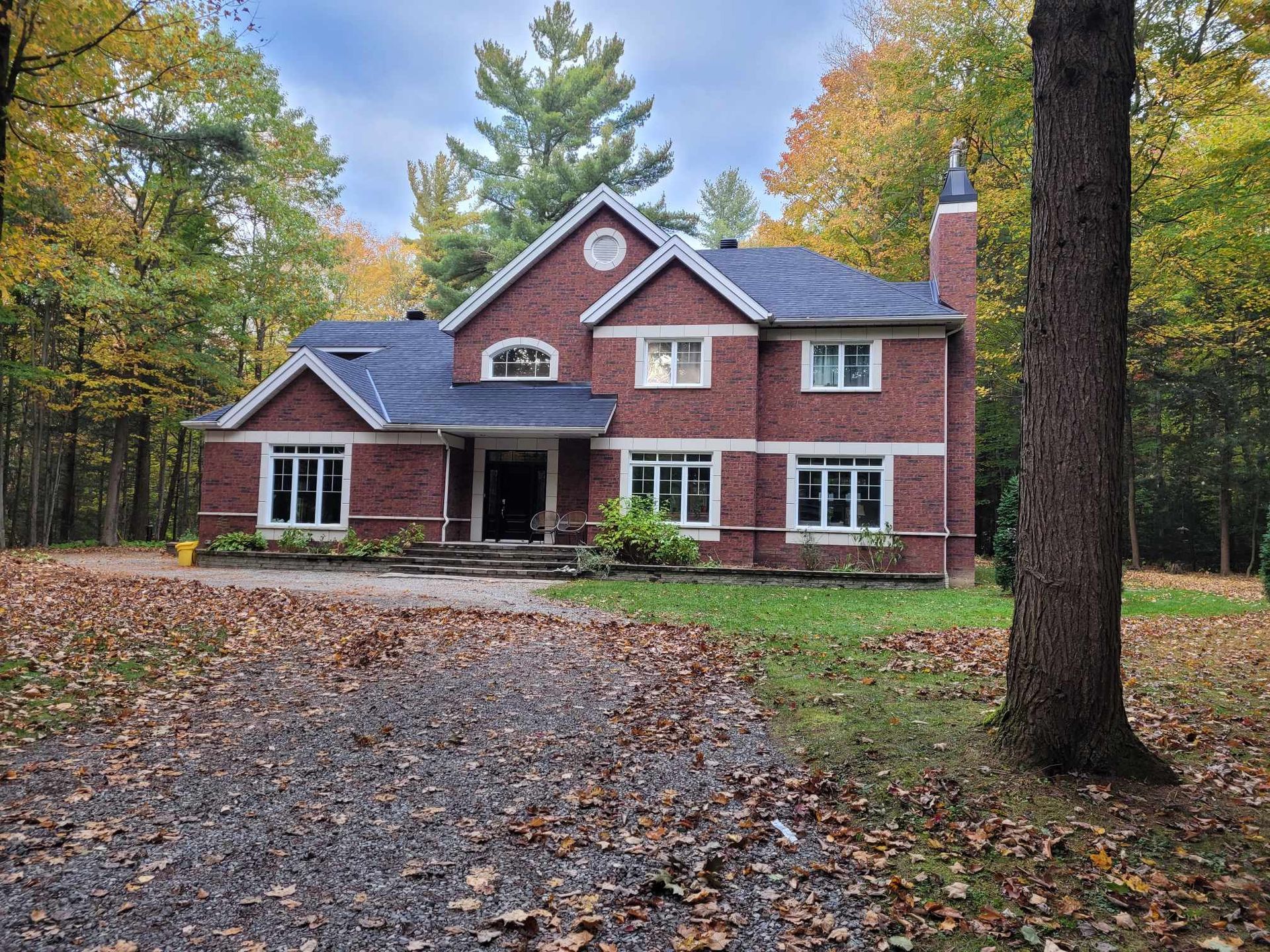 A large red brick house is surrounded by trees and leaves.