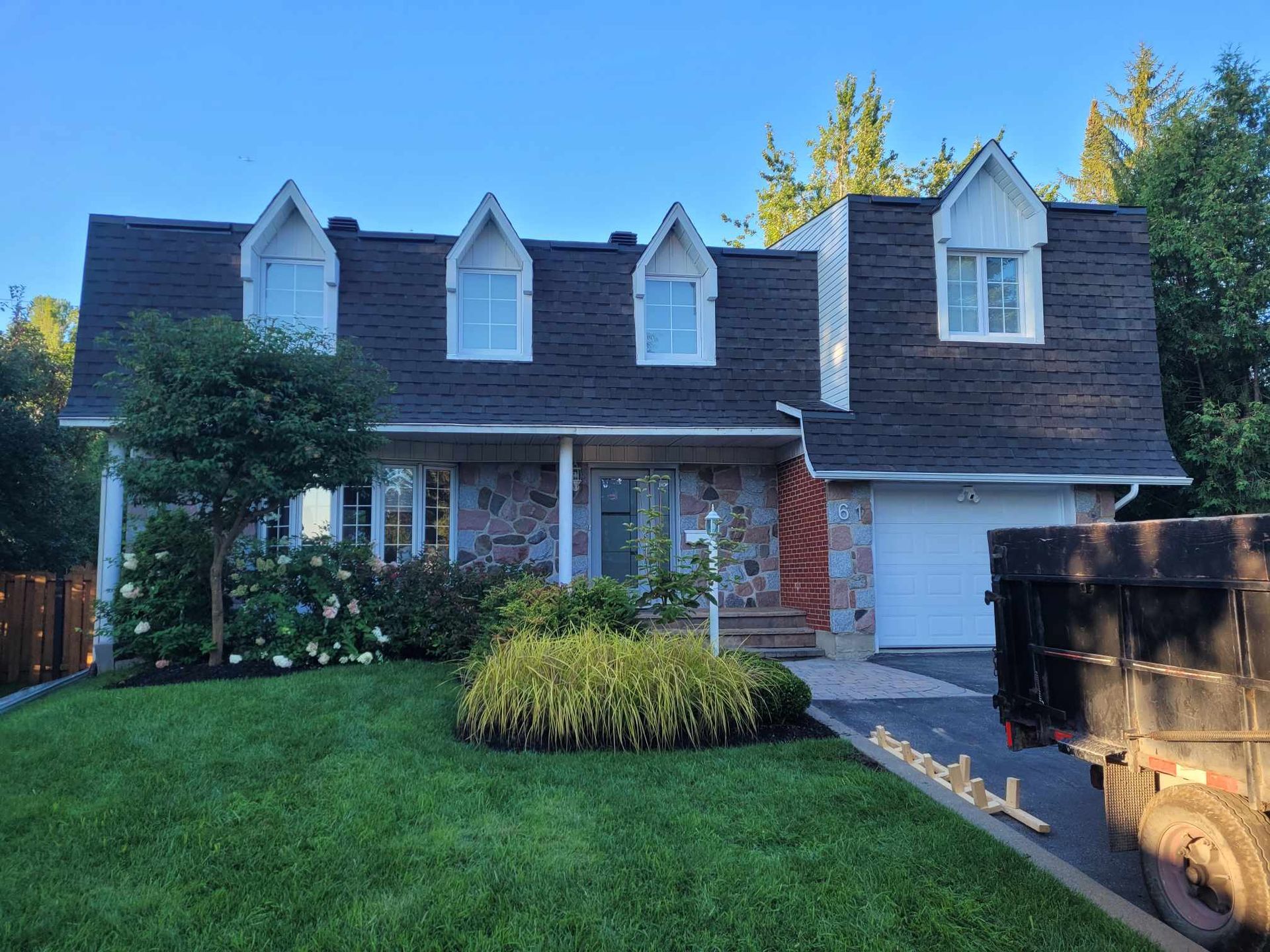 A large house with a black roof and white trim is sitting on top of a lush green lawn.