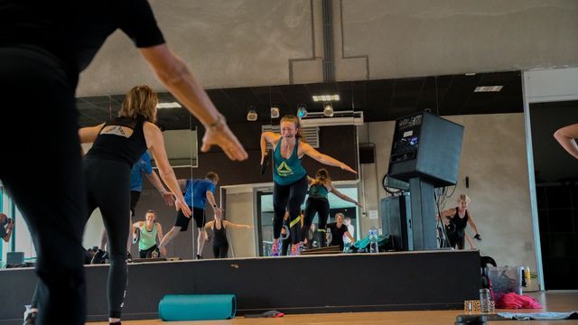 Mensen die sporten in een sportschool. Instructeur op de voorgrond, anderen op de achtergrond bezig met cardio.