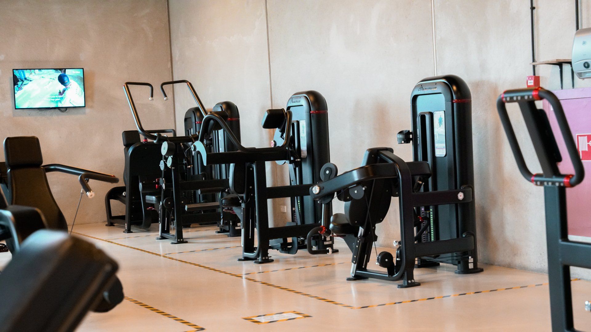 Een sportschool met veel fitnessapparatuur en een televisie aan de muur.