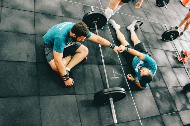 een man helpt een andere man een halter op te tillen in een sportschool.