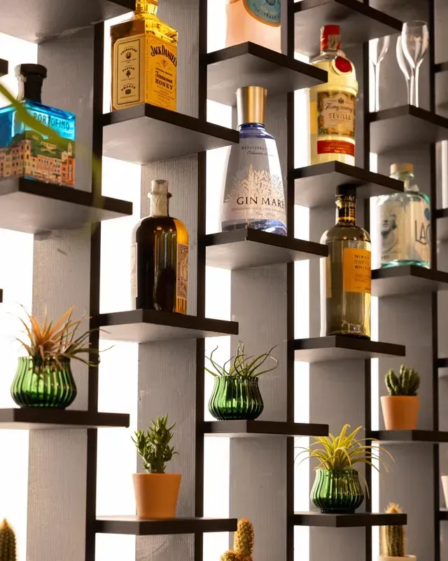 Scaffali con bottiglie di liquore e piccole piante in vaso disposte in una moderna composizione a parete.