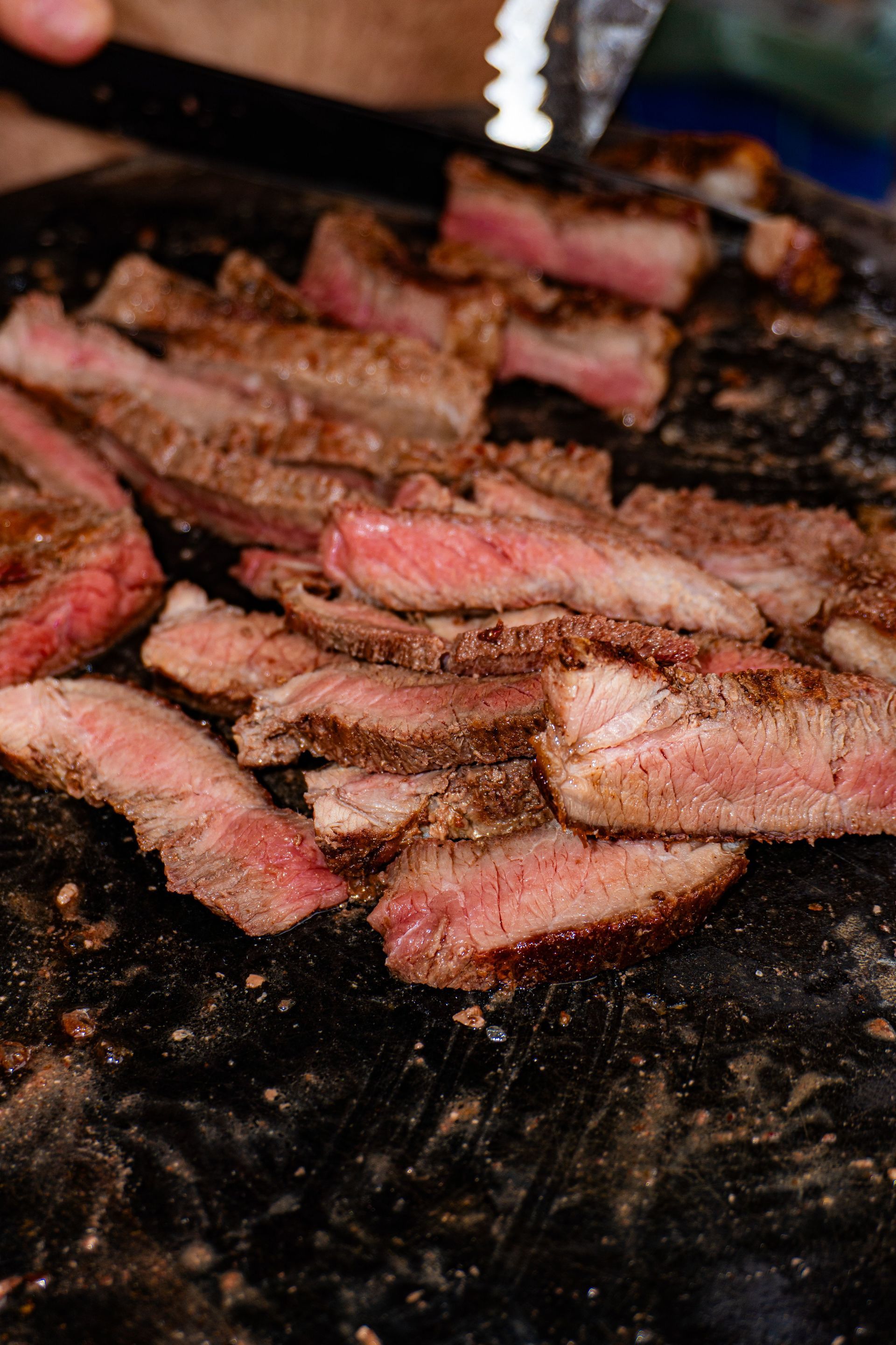 Fettine di bistecca al sangue che sfrigolano su una griglia rovente, con i bordi bruciacchiati e il centro rosato.