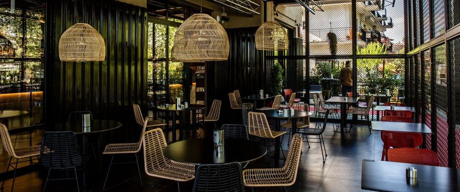 Interni moderni di un ristorante con sedie in vimini, divanetti rossi e lampade a sospensione intrecciate.