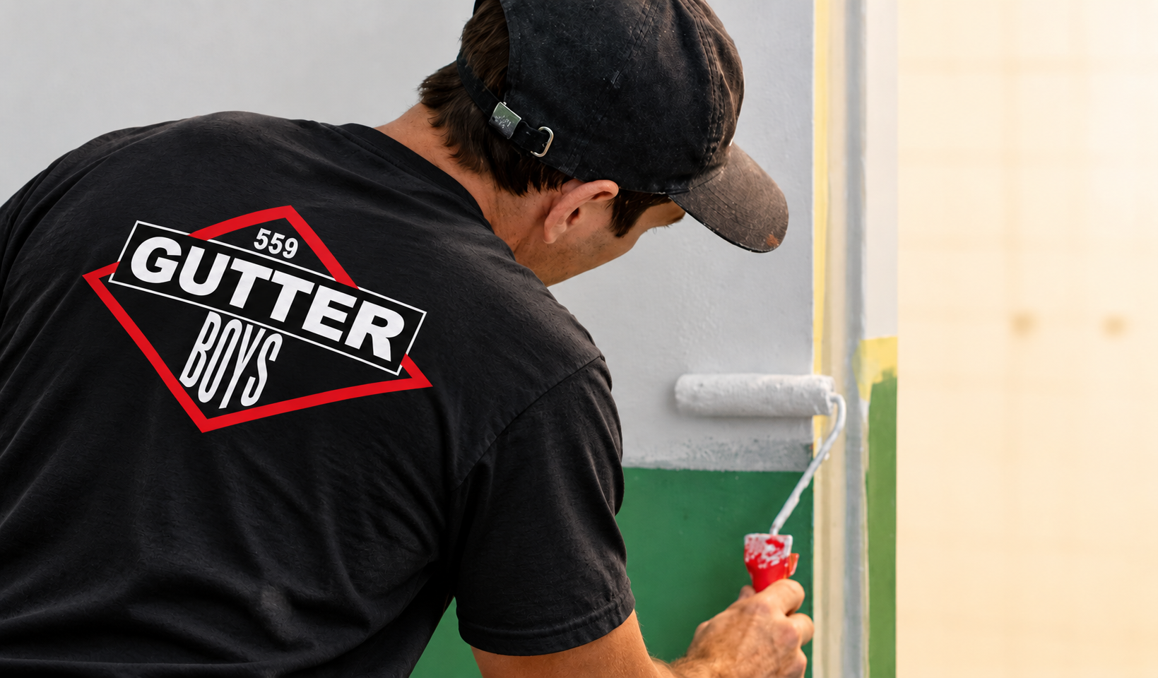 Worker painting a wall with a green roller, wearing a black shirt with a red-and-white logo.