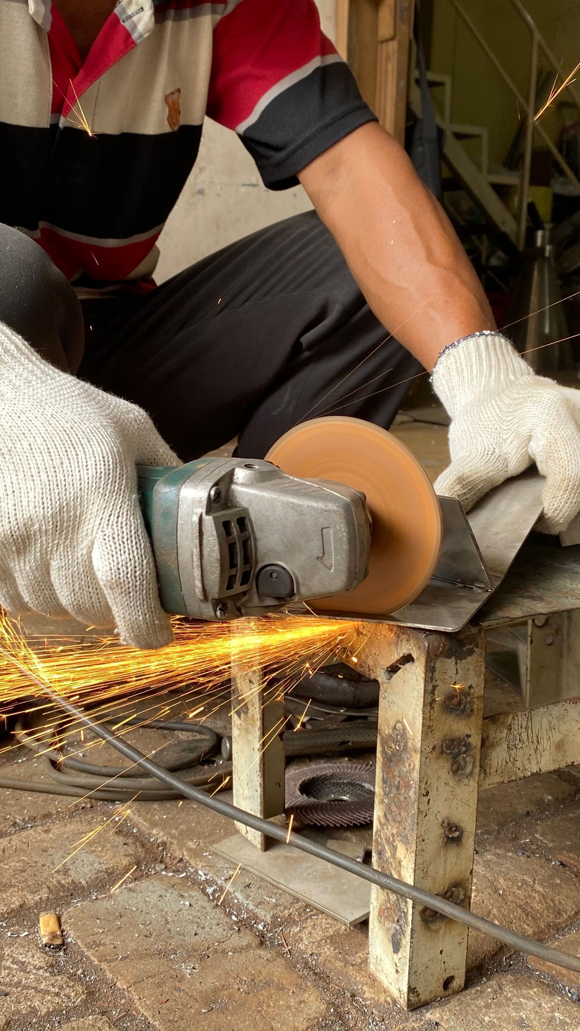 Worker using an angle grinder on metal, producing sparks in a workshop.