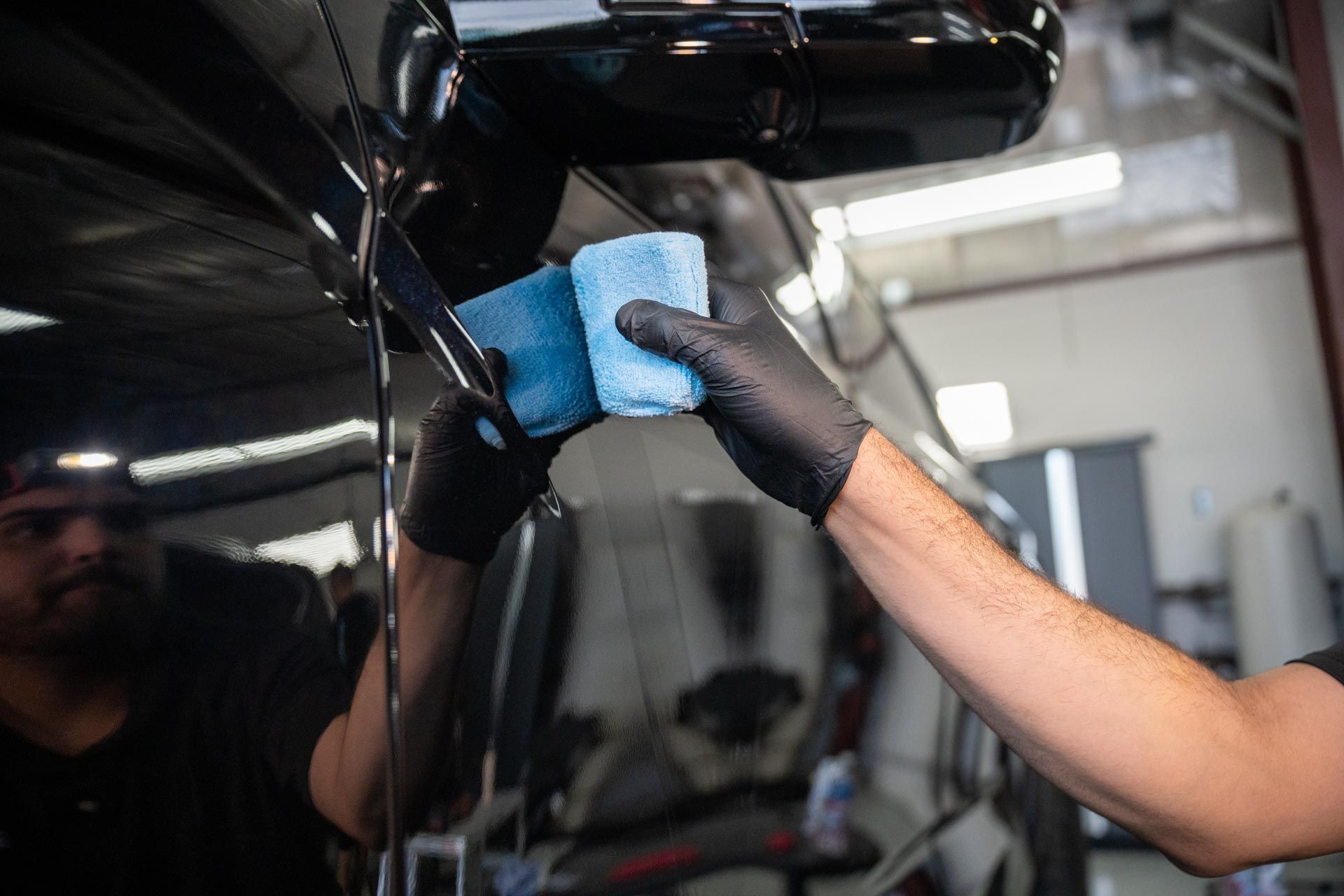 Person hand-washing a black car with a blue sponge in a garage