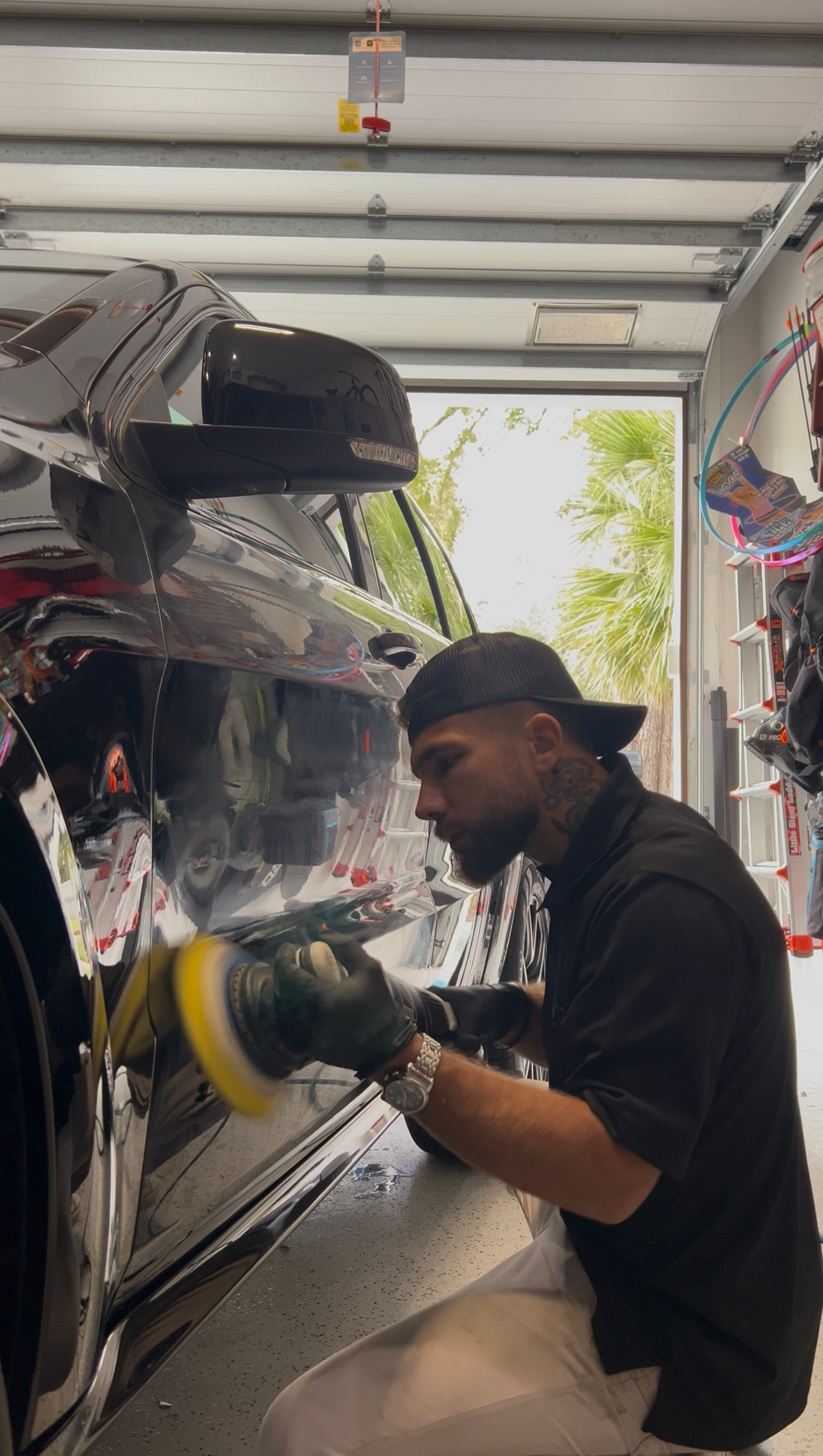 Man polishing a car in a garage, using a yellow buffer on the rear panel.