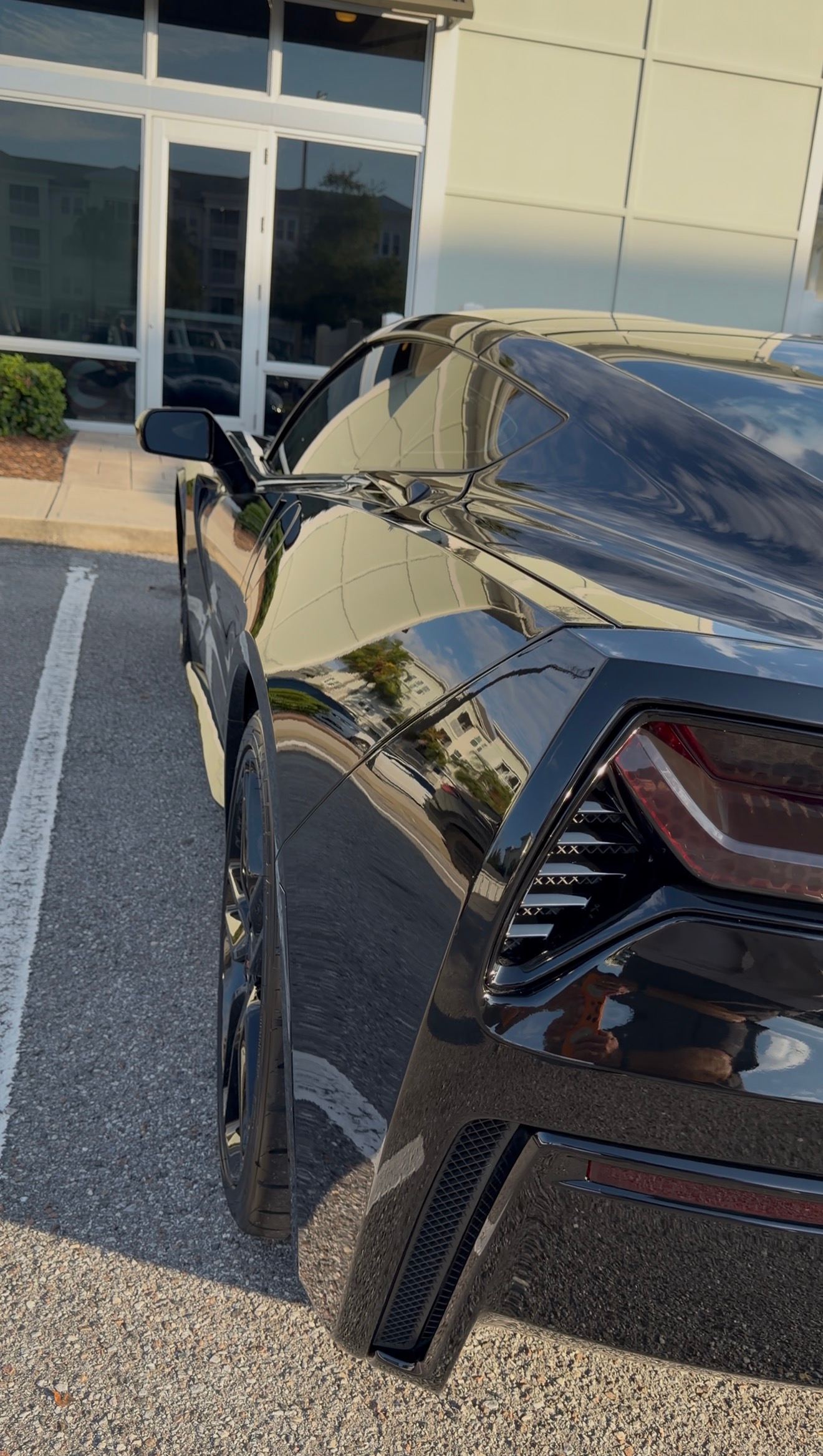 Black sports car parked outside a building, rear side damaged with a crumpled panel.