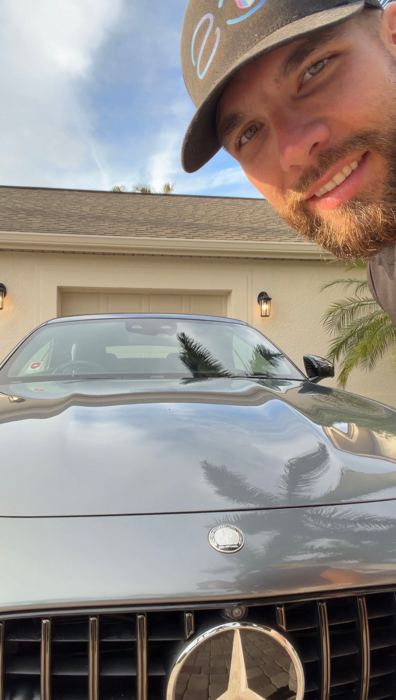 Smiling man in cap leaning beside a gray Mercedes SUV in a driveway