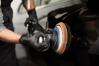 Hands polishing a black car wheel with a beige and blue buffing pad