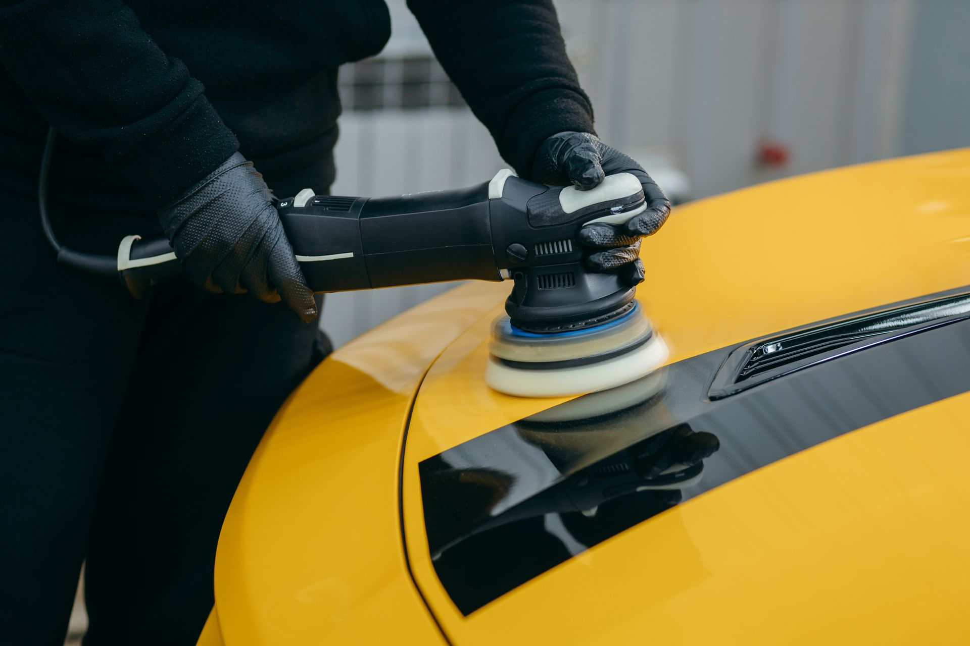 Person buffing a yellow car hood with a polishing tool