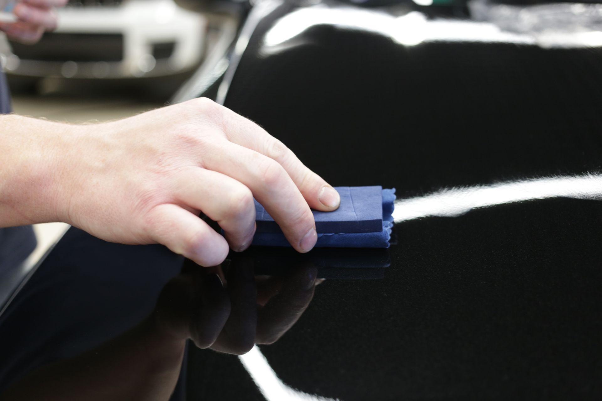 Hand polishing a glossy black car with a blue cloth