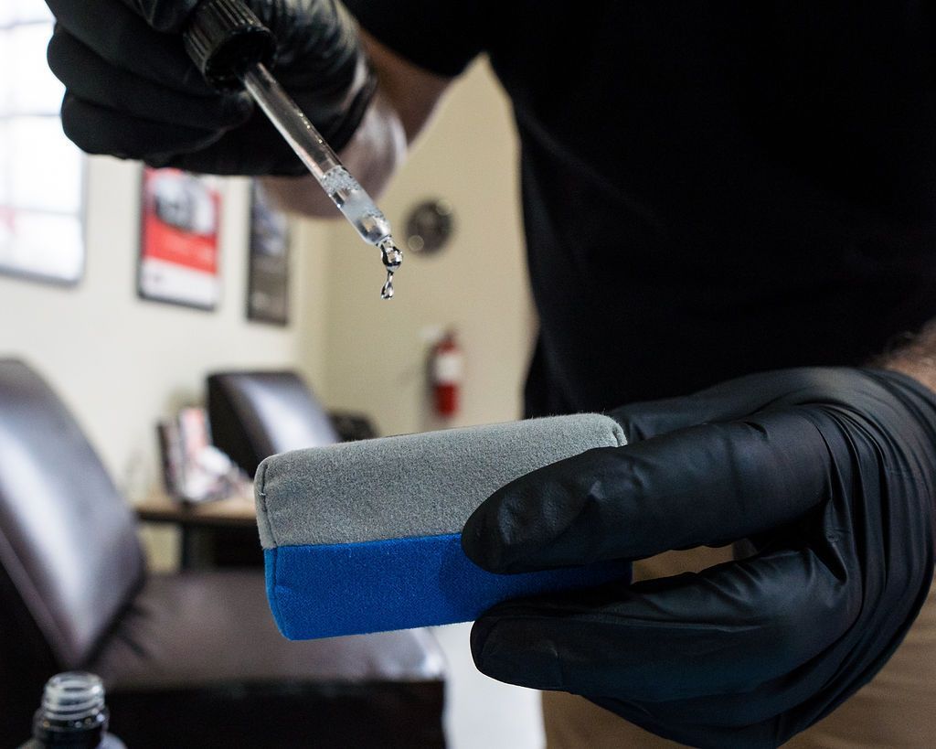 Gloved hands hold a sponge while a dropper adds liquid in a room with chairs in the background