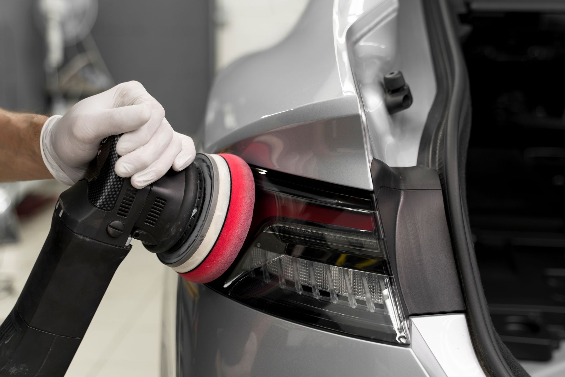 Gloved hands polishing a silver car tail light with a power buffer