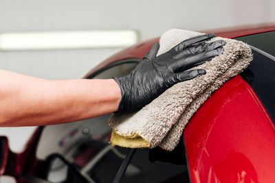 Gloved hand wiping red car with a microfiber cloth